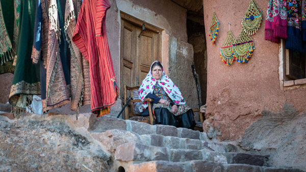 Abyaneh, Iran - May 2019: Iranian woman with traditional Abyaneh Persian dess sitting infront of her house in Abyahen, Iran