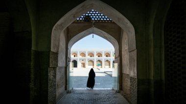 İsfahan, İran - Mayıs 2019: Kimliği belirlenemeyen siyah elbiseli İranlı kadın İsfahan Büyük Camii 'nin avlusuna doğru yürüyor.