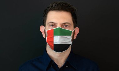 Birleşik Arap Emirlikleri bayraklı koruyucu tıbbi yüz maskesi takan adam. Endişeli ve endişeli görünüyor. Birleşik Arap Emirlikleri 'nde siyah arkaplanlı Coronavirus kavramı.