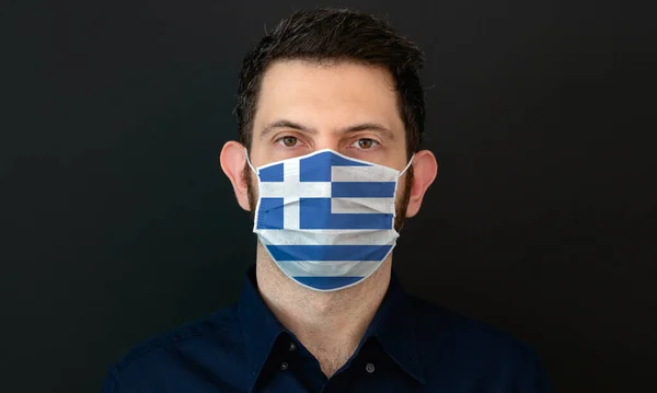Man wearing Greek flag protective medical face mask. He looks worried and concerned. Coronavirus concept in Greece with black background.