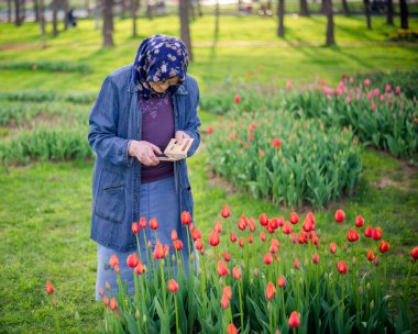 Kıdemli Müslüman kadın akıllı telefonuyla çiçeklerin fotoğrafını çekiyor. Yaşlı kadın mobil fotoğrafçılık konseptini kullanıyor..