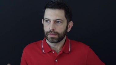 Adam bir sorunla ilgili kararsız, siyah arka planda kırmızı tişört giyiyor. Stüdyo çekimi. Karar verme ve kafa karıştırma kavramı.