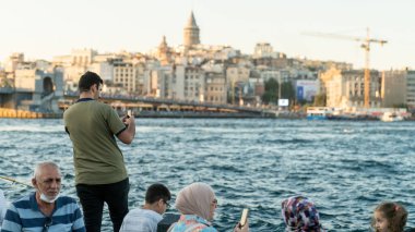 İstanbul, Türkiye - Eylül 2021: Eminonu limanında turistler ve yerel halk. İstanbul şehrinin fotoğrafını çeken bir turist. Galata kulesi güzel bir arka plan sağlar..