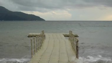 Yağmurlu bir günde dalgalı bir denizde yüzen plastik rıhtım. Dengesiz platform dalgalarla hareket ediyor, yürümeyi zorlaştırıyor..