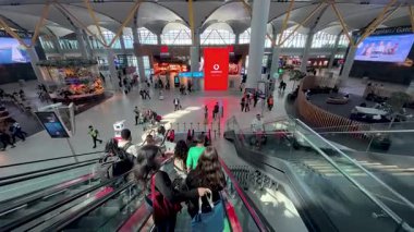İstanbul, Türkiye - 15 Eylül 2025: İstanbul Havalimanı 'nın modern terminalinde yürüyen merdivene inen yolcular, ferah kalkış salonu, perakende mağazaları, dijital ekranlar ve görünür mimari kemerler
