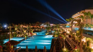 Fethiye, Türkiye - 12 Ekim 2025: Geceleyin XO Burnu Arnna 'daki lüks sahil beldesi turkuaz havuzları, palmiye ağaçları ve parıldayan mimariyle aydınlatılmış, zarif ve rahatlatıcı bir tropikal kaçışı çağrıştıran.