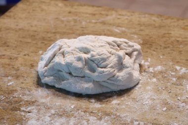 Una bulanmış çiğ pizza hamuru, mutfak tezgahında oturuyor..