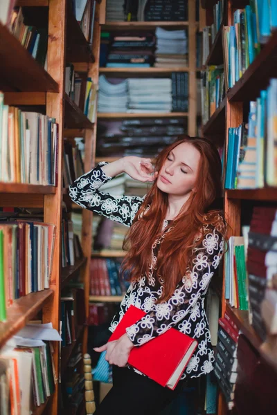 Mladá zrzka dívka v knihovně — Stock fotografie