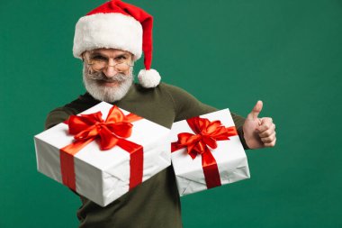 Sakallı, modern Noel Baba hediyeler taşıyor ve yeşil arka planda gülümsüyor.