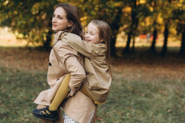Mutlu anne ve güzel kızı eğleniyor ve sonbahar parkında yürüyor..