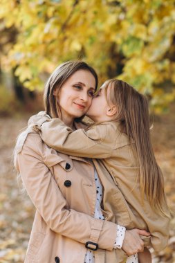 Mutlu anne ve güzel kızı eğleniyor ve sonbahar parkında yürüyor..