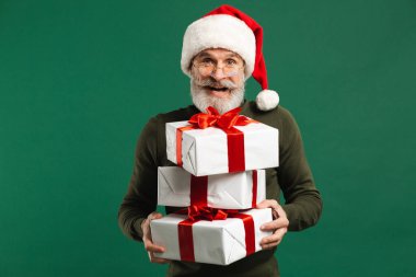 Sakallı, modern Noel Baba hediyeler taşıyor ve yeşil arka planda gülümsüyor.