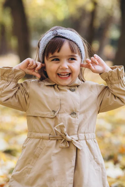 秋天的公园里 穿着米黄色外套的快乐而美丽的女孩流露出感情 用手指合上了耳朵 — 图库照片