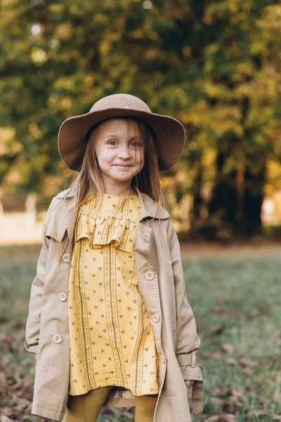 一个穿着黄色衣服和米黄色外套的小女孩在秋天的公园里散步 — 图库照片