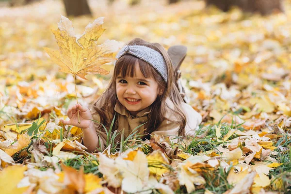 Szczęśliwa Piękna Dziewczynka Beżowym Płaszczu Leży Wśród Żółtych Liści Jesiennego — Zdjęcie stockowe