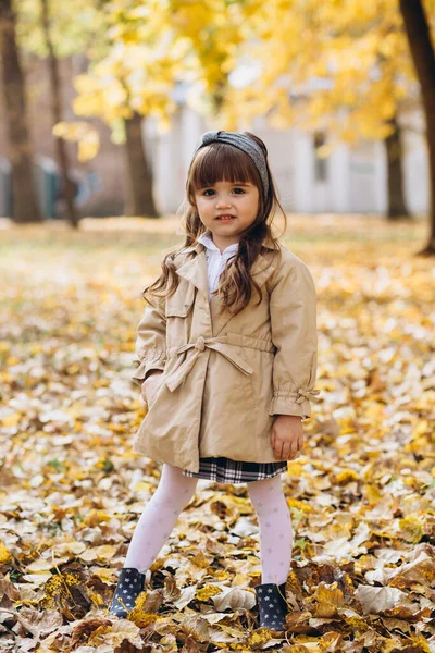 穿着米黄色外套的快乐而美丽的小女孩走在秋天的公园里 — 图库照片