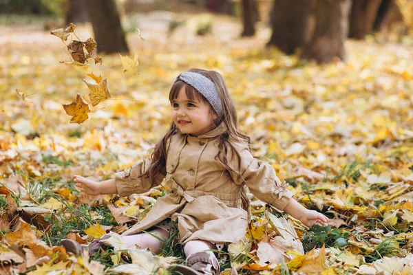 Szczęśliwa Piękna Dziewczynka Beżowym Płaszczu Siedząca Wśród Żółtych Liści Jesiennym — Zdjęcie stockowe