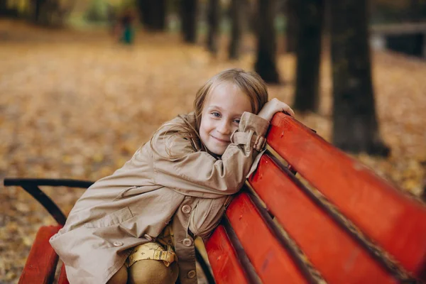 一个穿着黄色衣服和米黄色外套的小女孩在秋天的公园里散步 — 图库照片