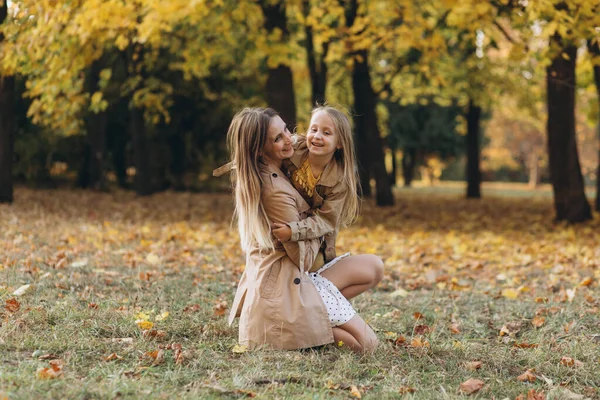 快乐的妈妈和她美丽的女儿坐在秋天的公园里 在黄叶间嬉戏 — 图库照片