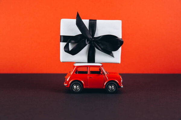 small toy car with gift box on red background