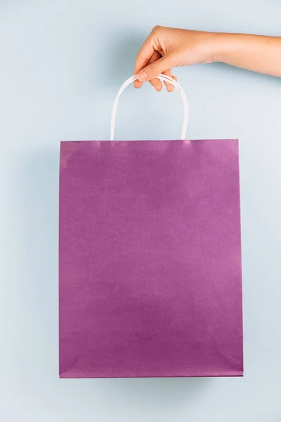 青地に分離された紫色の紙袋を持つ女性の手 — ストック写真