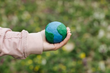 Female hands holding Earth in hands against green spring background.