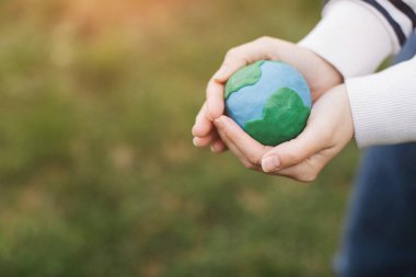 Female hands holding Earth in hands against green spring background.