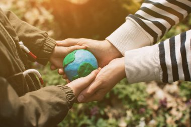 Mother and her daughter holding Earth in hands against green spring background.