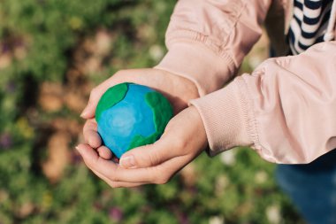 Female hands holding Earth in hands against green spring background.