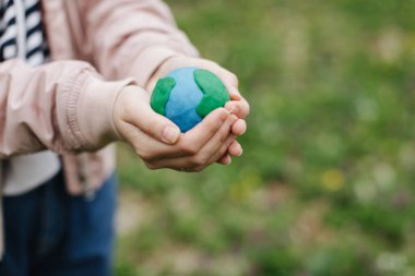 Female hands holding Earth in hands against green spring background.