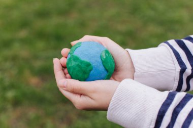 Female hands holding Earth in hands against green spring background.