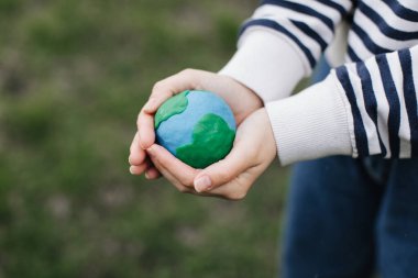 Female hands holding Earth in hands against green spring background.