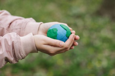 Female hands holding Earth in hands against green spring background.