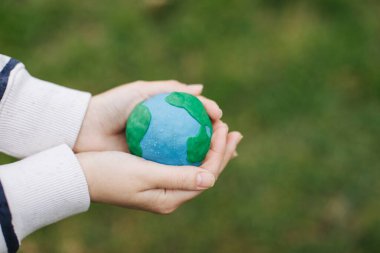 Female hands holding Earth in hands against green spring background.
