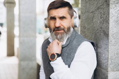 Sakallı, kır saçlı yaşlı adam temiz kentsel alanlarda müzik dinliyor.