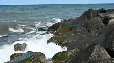 Dalgalar engebeli yosunlu taşlara çarpar. Her çarpışma dalgasında deniz köpüğü yukarıya doğru fışkırır. Güneş ışığı hareket eden suyu ve ıslak kayaları aydınlatır. Doğanın gücü sessiz bir güçle kayaya çarpar.