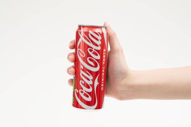 Bir insan eli uzun bir Coca-Cola kutusunu nazikçe beyaz bir stüdyo arka planına doğru tutar. Minimalist kompozisyon, klasik alkolsüz içeceğin etkileşimini, ölçeğini ve simgesel kırmızı markasını vurgular.