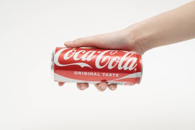 Bir insan eli uzun bir Coca-Cola kutusunu nazikçe beyaz bir stüdyo arka planına doğru tutar. Minimalist kompozisyon, klasik alkolsüz içeceğin etkileşimini, ölçeğini ve simgesel kırmızı markasını vurgular.