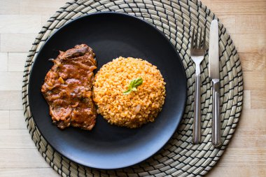 Biftek domates sosu ve bulgur pirinç siyah bir tabak içinde