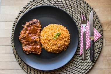 Biftek domates sosu ve bulgur pirinç siyah bir tabak içinde