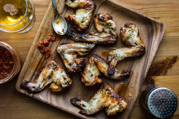 Asas de frango em uma placa de madeira com bebida e molho de tomate . — Fotografia de Stock