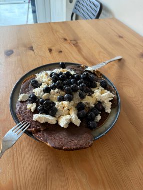 Yaban mersinli dökme demir tavada servis edilen ev yapımı süzme peynir protein krepleri.