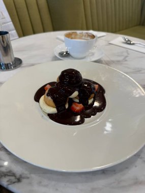 Restoranda servis edilen zengin, parlak, koyu çikolata soslu klasik profiteroller.