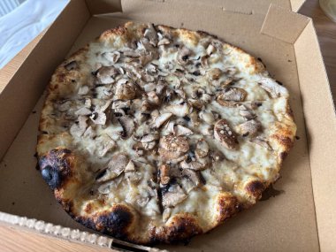 Mantarlı pizzayı ahşap bir masada yemeye hazır bir kutuda götür.