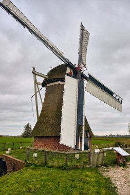 Visvliet, Hollanda; 11 Ekim 2025: Tarihsel polen değirmeni Hilmahuistermolen, Hollanda kırsal su yönetiminin sembolü olan bulutlu sonbahar gökyüzünün altında açık Groningen tarım arazisinde duruyor.