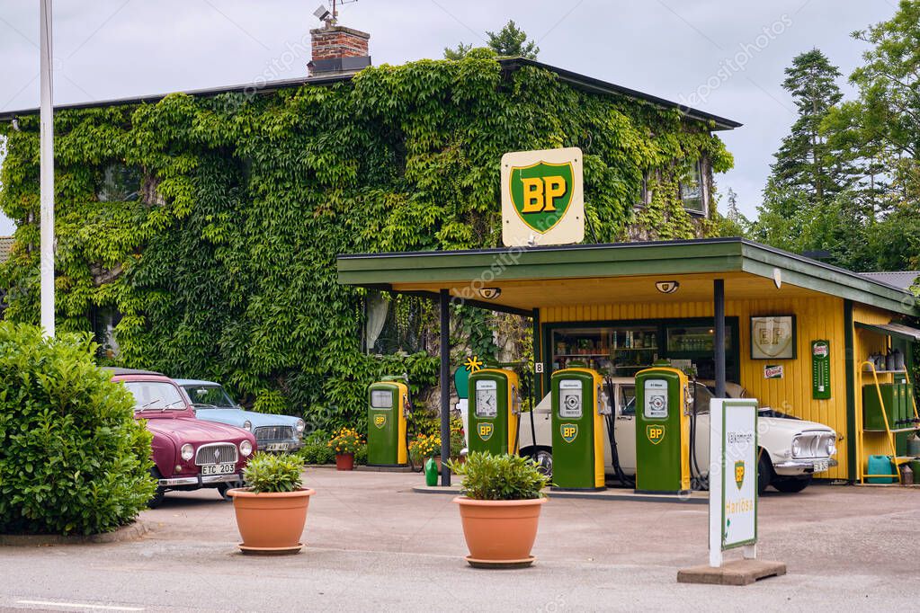 Harlosa, Sweden ; July 26, 2025: Vintage BP gas station with classic cars and retro fuel pumps in green and yellow, next to ivy-covered house, capturing nostalgic automotive heritage.