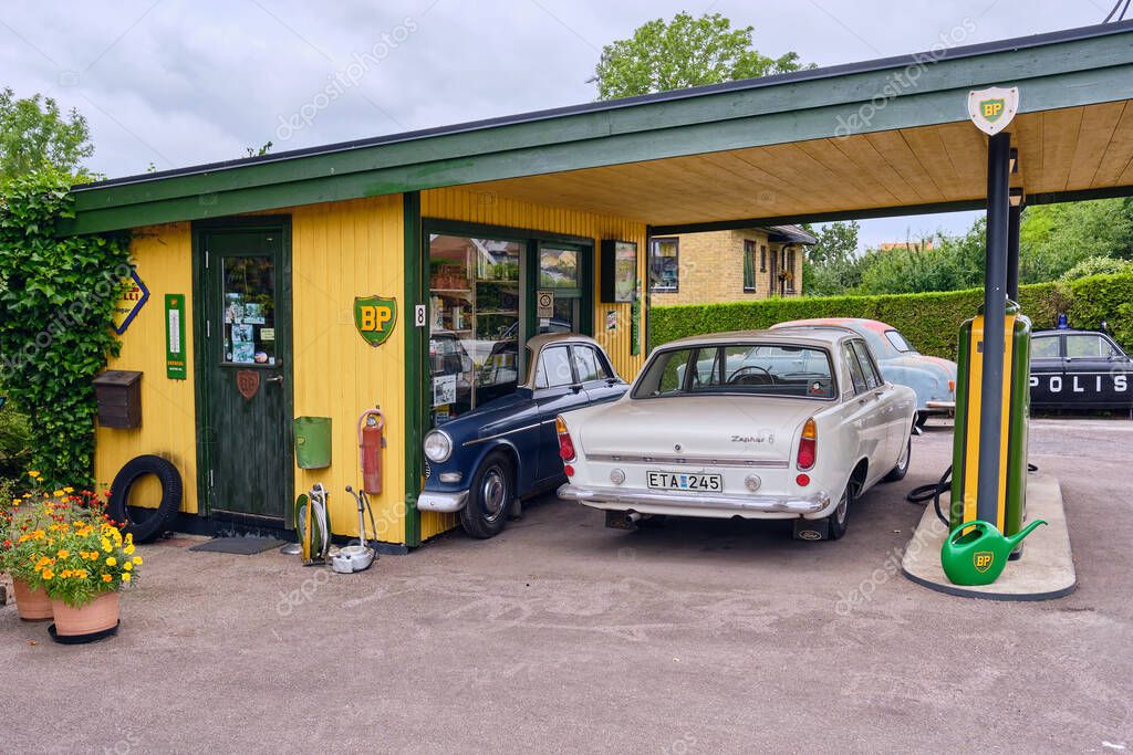 Harlosa, Sweden ; July 26, 2025: Vintage BP gas station with classic cars and retro fuel pumps in green and yellow, next to ivy-covered house, capturing nostalgic automotive heritage.