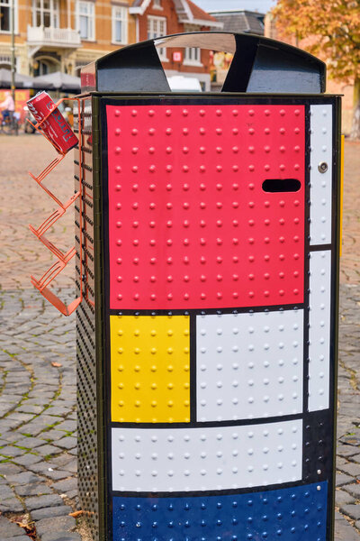 Winterswijk, Netherlands ; October 16, 2025: Modern trash can in Mondrian style with bold color blocks and side deposit tray for cans, placed on a public square promoting urban sustainability.