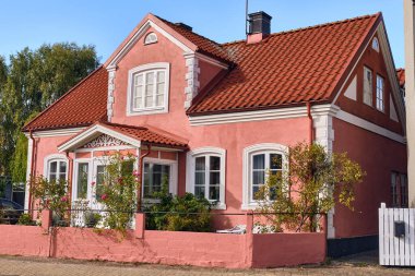 Ahus, İsveç; 22 Eylül 2025: İsveç 'in bir kentinin mimari mirası olarak sıcak güneş ışığında gösterilen, ana cadde boyunca beyaz süslemeli ve kırmızı kiremit kaplamalı büyüleyici pembe tuğla ev.
