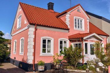 Ahus, İsveç; 22 Eylül 2025: İsveç 'in bir kentinin mimari mirası olarak sıcak güneş ışığında gösterilen, ana cadde boyunca beyaz süslemeli ve kırmızı kiremit kaplamalı büyüleyici pembe tuğla ev.